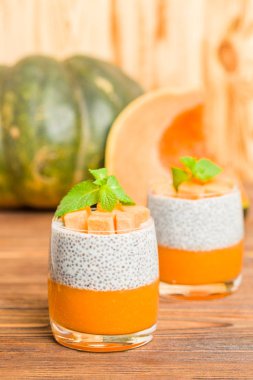 Chia puding güzel gözlük yeşil nane yaprakları ve kahverengi ahşap arka plan - ham vejetaryen tatlı sağlıklı organik tatlı taze olgun sebze ile kabak püresi ile.