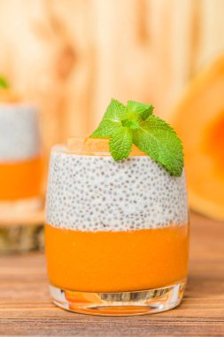 Chia puding güzel gözlük yeşil nane yaprakları ve kahverengi ahşap arka plan - ham vejetaryen tatlı sağlıklı organik tatlı taze olgun sebze ile kabak püresi ile.