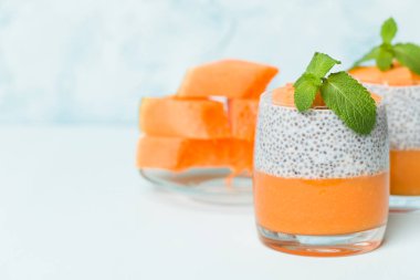 Chia tohum puding kabak ile güzel gözlük yeşil nane yaprakları ile püre ve pastel mavi arka plan - ham vejetaryen şekerli organik tatlı taze olgun turuncu sebze kesme.