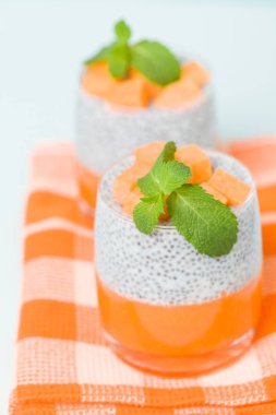 Chia tohum puding kabak ile güzel gözlük yeşil nane yaprakları ile püre ve pastel mavi arka plan - ham vejetaryen şekerli organik tatlı taze olgun turuncu sebze kesme.