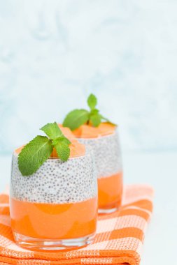 Chia tohum puding kabak ile güzel gözlük yeşil nane yaprakları ile püre ve pastel mavi arka plan - ham vejetaryen şekerli organik tatlı taze olgun turuncu sebze kesme.