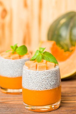 Chia puding güzel gözlük yeşil nane yaprakları ve kahverengi ahşap arka plan - ham vejetaryen tatlı sağlıklı organik tatlı taze olgun sebze ile kabak püresi ile.