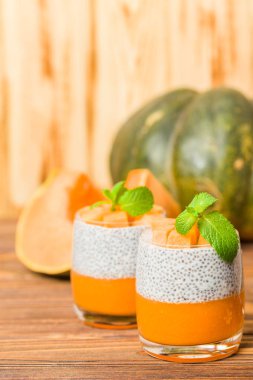 Chia puding güzel gözlük yeşil nane yaprakları ve kahverengi ahşap arka plan - ham vejetaryen tatlı sağlıklı organik tatlı taze olgun sebze ile kabak püresi ile.