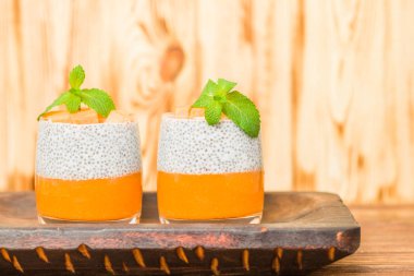 Chia puding güzel gözlük yeşil nane yaprakları ve kahverengi ahşap arka plan - ham vejetaryen tatlı sağlıklı organik tatlı taze olgun sebze ile kabak püresi ile.