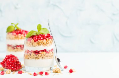 Nar parfe - granola pul, yoğurt ve olgun meyve şekerli organik katmanlı tatlı güzel gözlük kopya alanı pastel mavi zemin üzerine tohum. Doğal vejetaryen sağlıklı gıda.