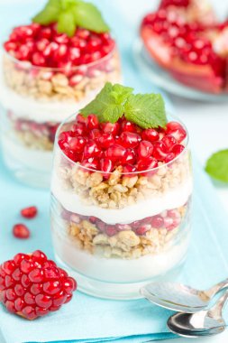 Nar parfe - granola pul ile şekerli organik katmanlı tatlı, güzel gözlük pastel mavi zemin üzerine yoğurt ve kırmızı olgun meyve tohumları. Doğal vejetaryen sağlıklı gıda.