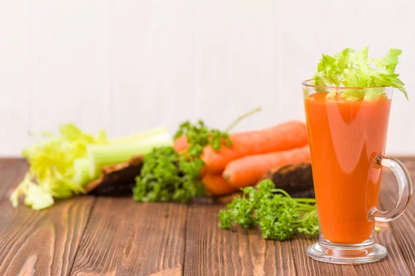 Carrot and celery juice with fresh vegetables on bark plates on wooden background - raw vegetarian vitamin drink for healthy eating concept. Organic food and beverage decorated with parsley leaves.