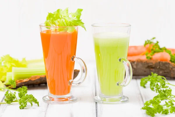 Carrot and celery juice with fresh vegetables on bark plates on wooden background - raw vegetarian vitamin drink for healthy eating concept. Organic food and beverage decorated with parsley leaves.