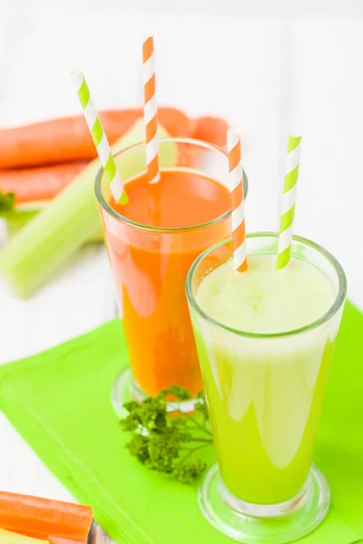 Carrot and celery juice with fresh vegetables on bark plates on wooden background - raw vegetarian vitamin drink for healthy eating concept. Organic food and beverage decorated with parsley leaves.