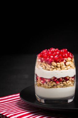 Nar parfe - granola pul, yoğurt ve olgun meyve şekerli organik katmanlı tatlı güzel gözlük kopya alanı siyah zemin üzerine tohum. Karanlık ruh tarzı doğal sağlıklı gıda.