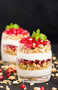 Nar parfe - granola pul, yoğurt ve olgun meyve şekerli organik katmanlı tatlı güzel gözlük kopya alanı siyah zemin üzerine tohum. Karanlık ruh tarzı doğal sağlıklı gıda.
