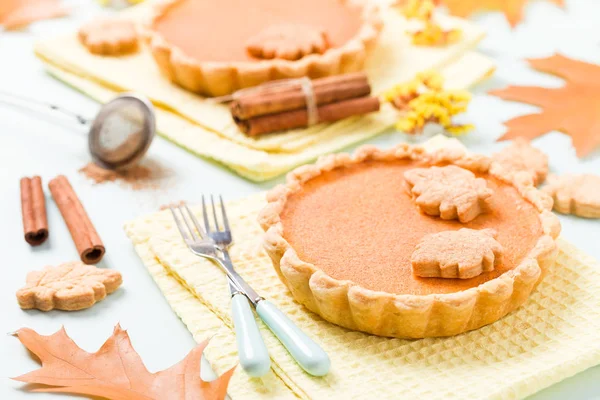 Pumpkin pie with cinnamon and cookies on yellow napkins on pastel blue background with autumn yellow leaves - top view close up photography of seasonal american traditional sweet baked food.