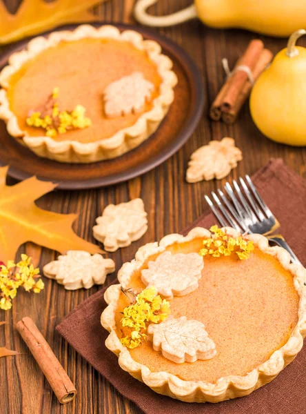 Pumpkin pie with cinnamon and cookies on brown napkins on wooden background with autumn yellow leaves - top view close up photography of seasonal american traditional sweet baked food.