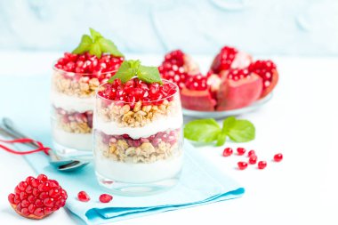 Nar parfe - granola pul ile şekerli organik katmanlı tatlı, güzel gözlük pastel mavi zemin üzerine yoğurt ve kırmızı olgun meyve tohumları. Doğal vejetaryen sağlıklı gıda.