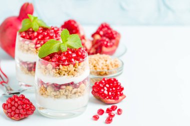 Nar parfe - granola pul, yoğurt ve olgun meyve şekerli organik katmanlı tatlı güzel gözlük kopya alanı pastel mavi zemin üzerine tohum. Doğal vejetaryen sağlıklı gıda.