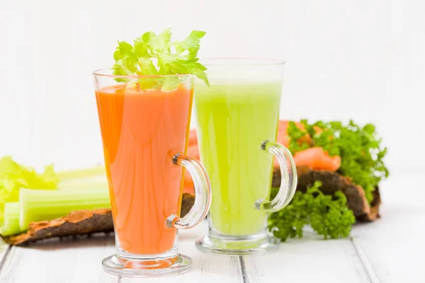 Carrot and celery juice with fresh vegetables on bark plates on wooden background - raw vegetarian vitamin drink for healthy eating concept. Organic food and beverage decorated with parsley leaves.