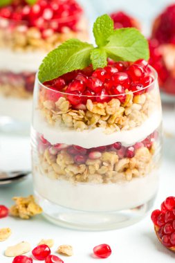 Nar parfe - granola pul ile şekerli organik katmanlı tatlı, güzel gözlük pastel mavi zemin üzerine yoğurt ve kırmızı olgun meyve tohumları. Doğal vejetaryen sağlıklı gıda.