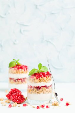 Nar parfe - granola pul, yoğurt ve olgun meyve şekerli organik katmanlı tatlı güzel gözlük kopya alanı pastel mavi zemin üzerine tohum. Doğal vejetaryen sağlıklı gıda.