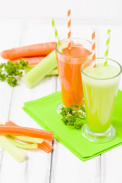 Carrot and celery juice with fresh vegetables on bark plates on wooden background - raw vegetarian vitamin drink for healthy eating concept. Organic food and beverage decorated with parsley leaves.