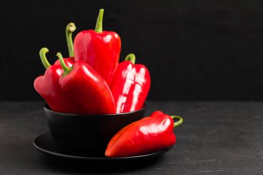 Siyah arka plan - bütün taze olgun tatlı sebze organik sağlıklı gıda kavramı için modern karanlık ruh tarzında closeup fotoğraf tabağa içinde kırmızı biber.