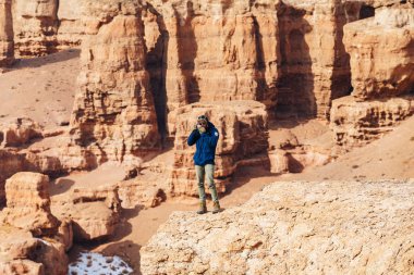 Bir kamera ile neşeli bir gezgin Kazakistan'daki Çarın Kanyonu'uçurumun kenarında duruyor. 
