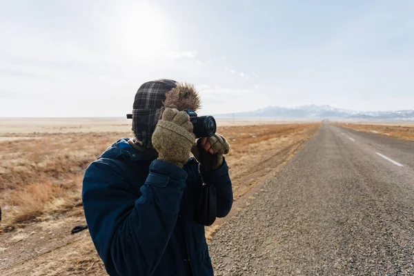 Un viaggiatore allegro con una macchina fotografica si trova sulla strada nella steppa kazaka completamente solo — Foto Stock