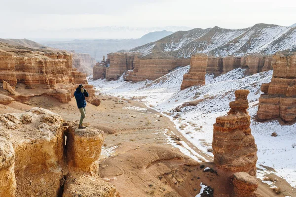 Een vrolijke reiziger met een camera staat aan de rand van de klif in de canyon van de Charyn in Kazachstan. Analogon van de Amerikaanse Grand Canyon Stockafbeelding