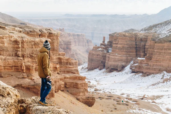 Een vrolijke reiziger met een camera staat aan de rand van de klif in de canyon van de Charyn in Kazachstan. Analogon van de Amerikaanse Grand Canyon Stockfoto