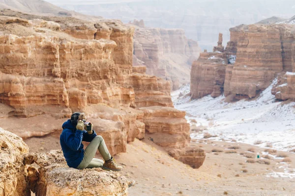 Een vrolijke reiziger met een camera zit op de rand van een klif in de canyon van de Charyn in Kazachstan. Analogon van de Amerikaanse Grand Canyon Rechtenvrije Stockafbeeldingen