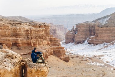 Bir kamera ile neşeli bir gezgin Çarın Kanyonu Kazakistan'ın ' bir uçurumun kenarına oturur. Analog Amerikan Grand Canyon