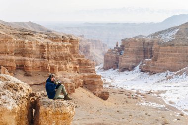 Bir kamera ile neşeli bir gezgin Çarın Kanyonu Kazakistan'ın ' bir uçurumun kenarına oturur. Analog Amerikan Grand Canyon