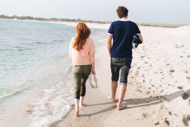 Genç bir çift çıplak ayakla boş bir plaj kumsalda yürürken