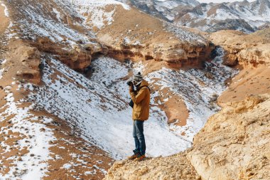 Bir kamera ile neşeli bir gezgin Kazakistan'daki Çarın Kanyonu'uçurumun kenarında duruyor.
