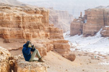 Bir kamera ile neşeli bir gezgin Çarın Kanyonu Kazakistan'ın ' bir uçurumun kenarında oturur.