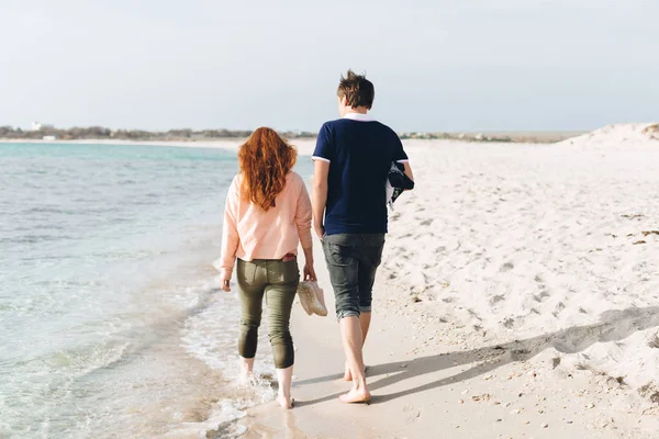 A young couple walking barefoot on the sand on an empty beach