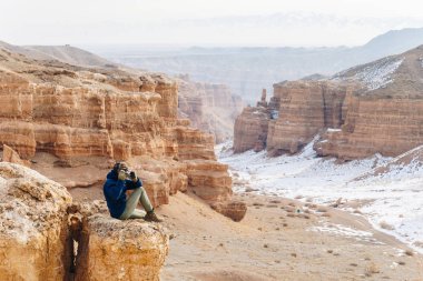 Bir kamera ile neşeli bir gezgin Çarın Kanyonu Kazakistan'ın ' bir uçurumun kenarında oturur.