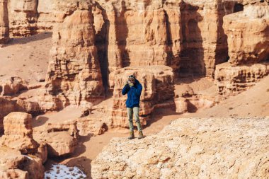Bir kamera ile neşeli bir gezgin Kazakistan'daki Çarın Kanyonu'uçurumun kenarında duruyor.