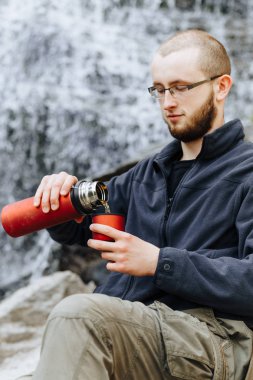 Genç bir adam üzerinden bir şelale oturan bir termos kahve veya çay dökülen