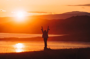 Dağlar ve deniz arka planı bir taş üzerinde gün batımını izlemek kız.