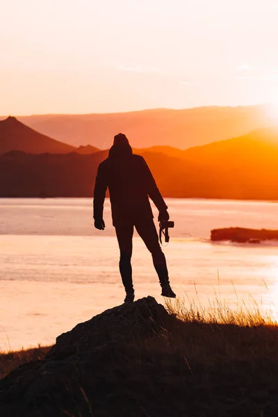 Viaggiatore maschile si trova da solo al tramonto sullo sfondo di acqua e montagne — Foto Stock