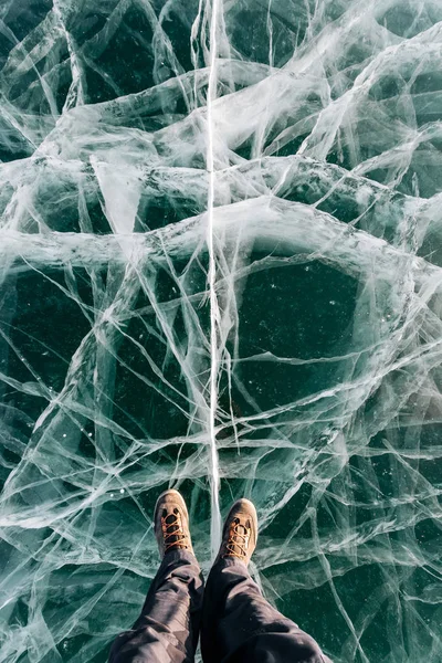 Voeten in de kofferbak staan op de groene ijs met enorme scheuren Stockfoto