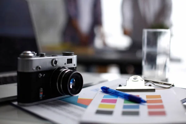 Laptop and camera on the desk in office, people standing on background