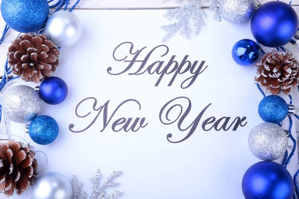 Texto feliz año nuevo en papel con árbol de piel, ramas, bolas de vidrio de colores, decoración y conos sobre un fondo de madera — Foto de Stock