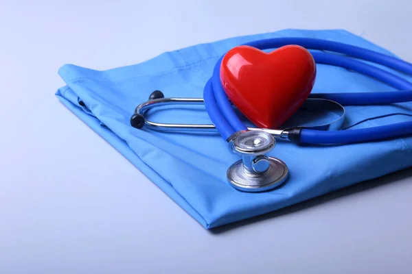 Manteau de médecin avec stéthoscope médical et coeur rouge sur le bureau — Photo