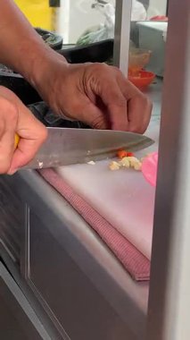 Ahşap bir tahtanın üzerinde kırmızı bir biberi bıçakla kesen bir şefin yakın çekimi. Bıçakla acı biber dilimlemek.