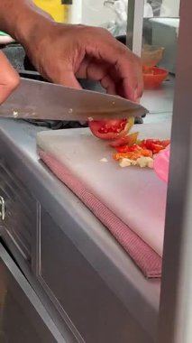 Ahşap bir tahtanın üzerinde kırmızı bir biberi bıçakla kesen bir şefin yakın çekimi. Bıçakla acı biber dilimlemek.