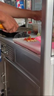 Ahşap bir tahtanın üzerinde kırmızı bir biberi bıçakla kesen bir şefin yakın çekimi. Bıçakla acı biber dilimlemek.