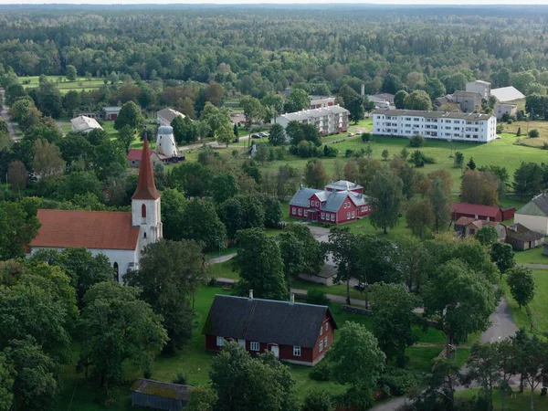 Mustjala, Estonya-12 Eylül 2025: Küçük bir kırsal köyün özünü yakalayan hava manzarası, bir kilise, geleneksel evler, bereketli alanlar ve sık orman manzarası ortaya çıkarıyor.