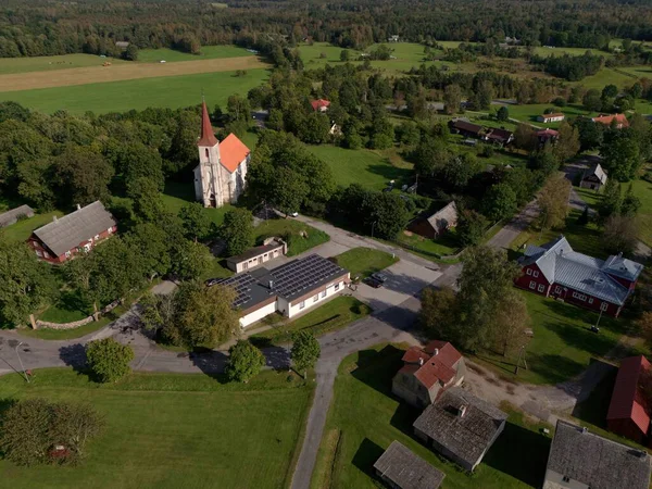 Mustjala, Estonya-12 Eylül 2025: Sıcak yaz güneşi altında bir kilise, güneş panelli evler ve bereketli manzaralarla dolu pitoresk bir köy ele geçirmek