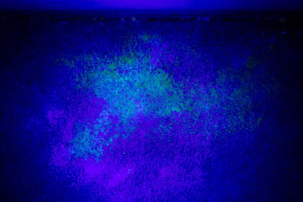 Black light illuminating a spot where a male cat keeps spraying pee.  The yellow green is the spray, the pink and light blue is where baking soda has been used to attempt to clean the spot before the cat resprayed.